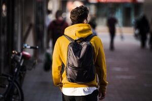 man in yellow and black backpack walking on sidewalk during daytime