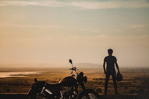 person standing besides motorcycle across grassland during dusk
