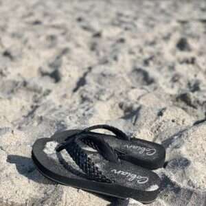 black flip flop on white sand during daytime